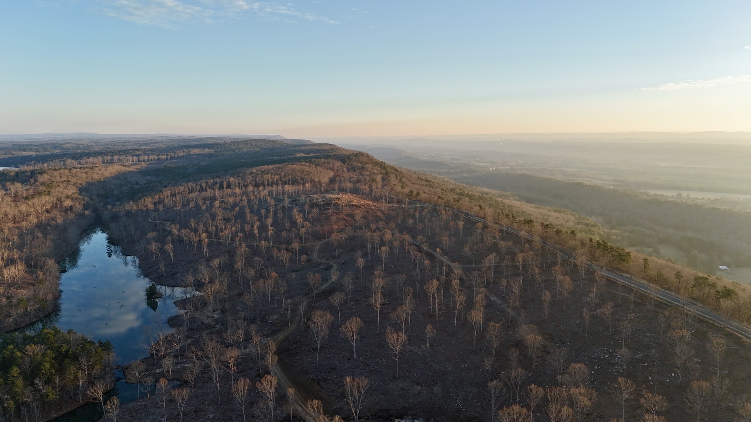 Signature panoramic aerial view across the Cairnwood lake, wooded slopes, road, and Lookout Mountain horizon in warm evening light